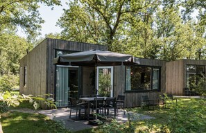 Une cabane moderne en bois dotée d’une terrasse, de grandes fenêtres et d’un espace extérieur aménagé et abrité.