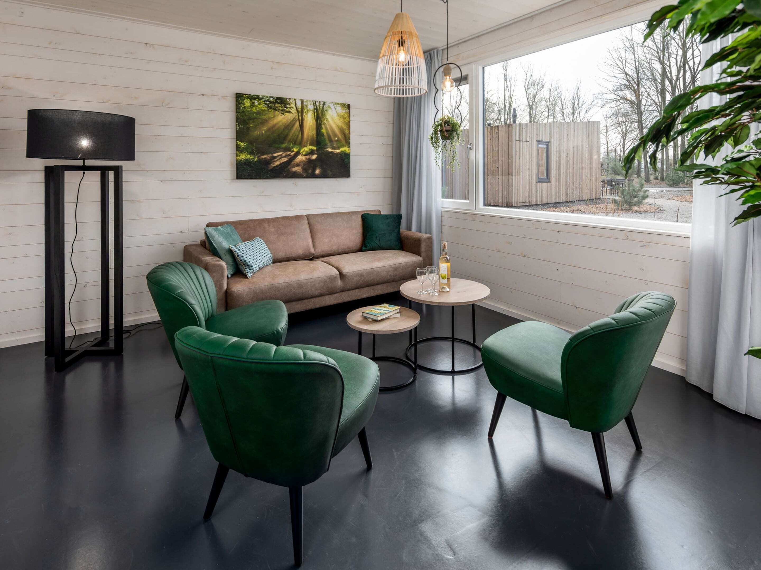 Ein modernes Wohnzimmer mit einer Couch, zwei grünen Sesseln, einem Couchtisch und einer Stehlampe.