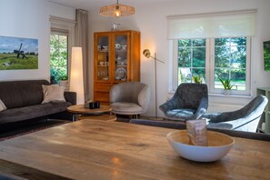 A living room with a sofa, armchairs, a wooden coffee table, a cabinet with glass doors, a floor lamp, and a window with a view of greenery. - Rustic Villa w/ Shared Pool (Paasloo)