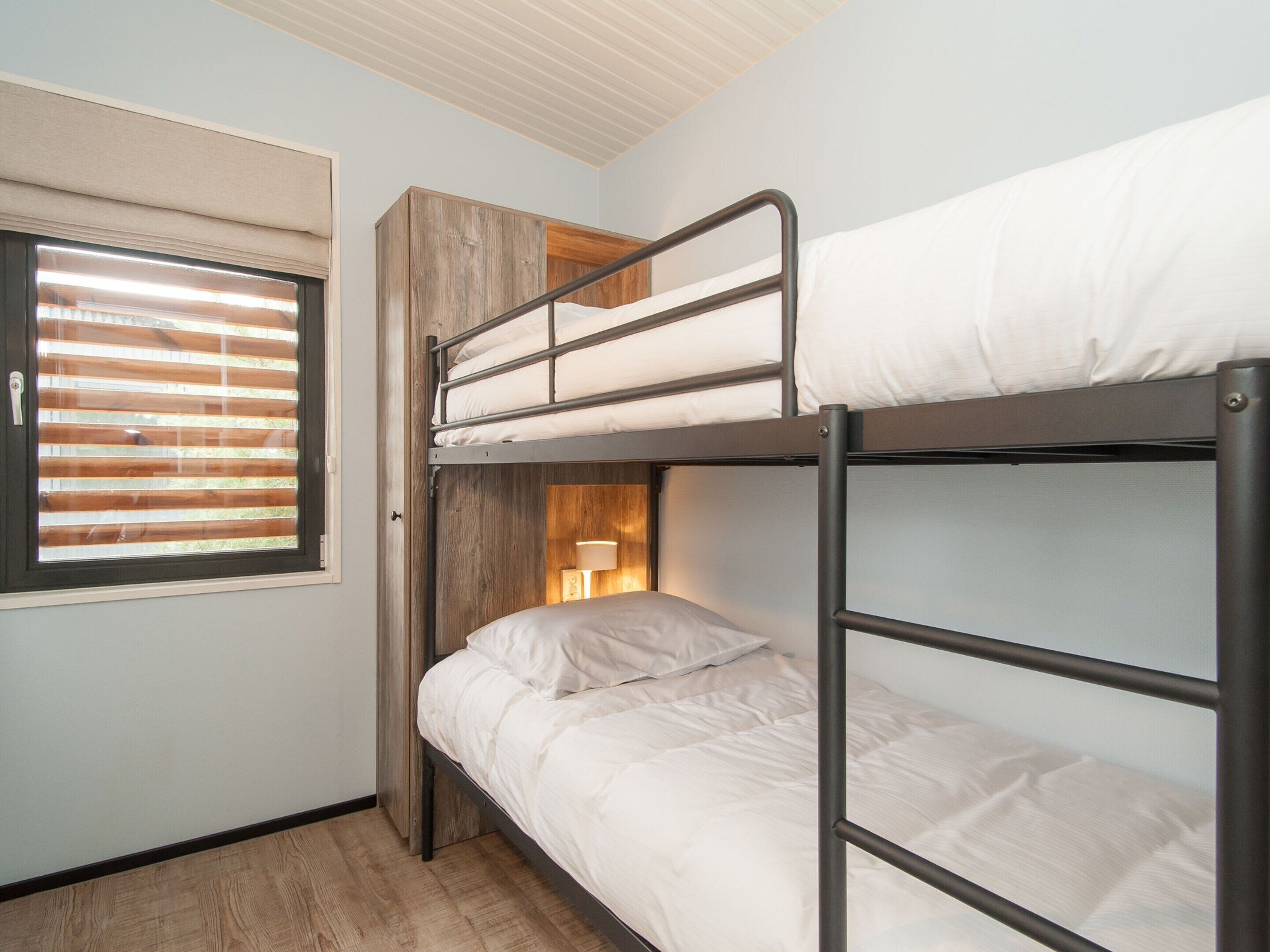 A bunk bed room with a window, wooden paneling, and a bedside lamp.