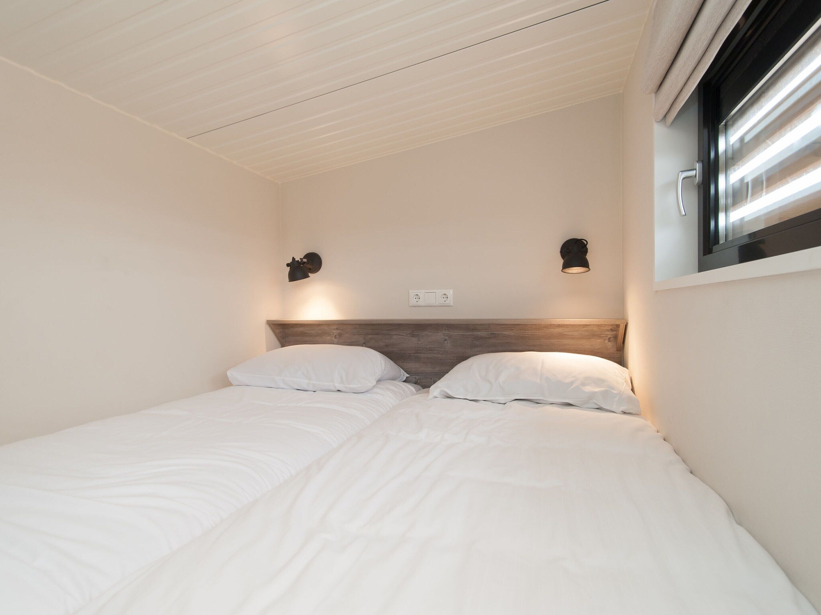 Une chambre à coucher avec une tête de lit en bois, deux lampes de chevet et une fenêtre avec des stores.