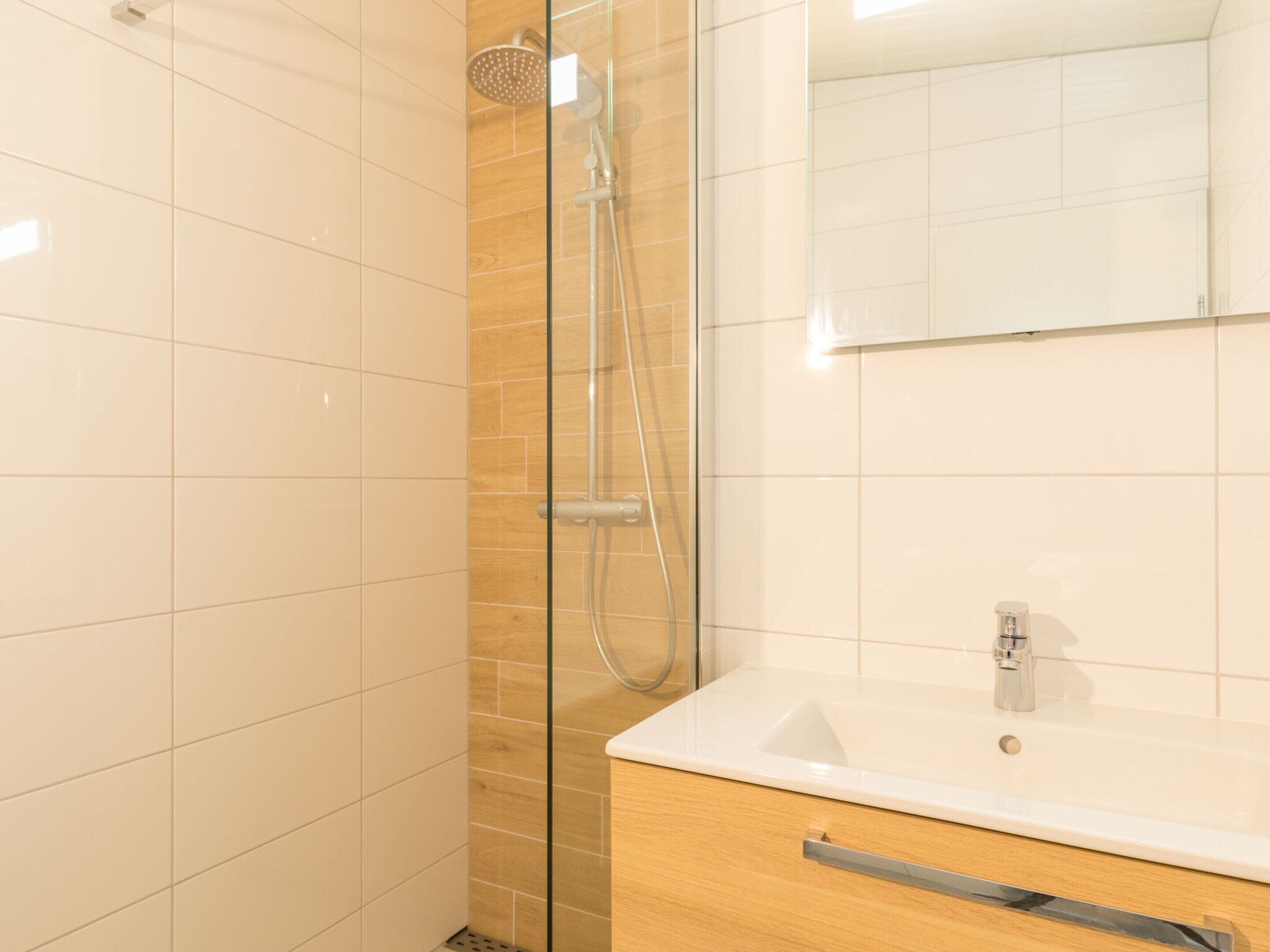 A modern bathroom with a glass shower enclosure, a white sink, and a wooden vanity.