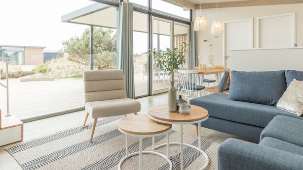 Un salon moderne comprenant un canapé, des fauteuils, une petite table et une grande fenêtre donnant sur l’extérieur.