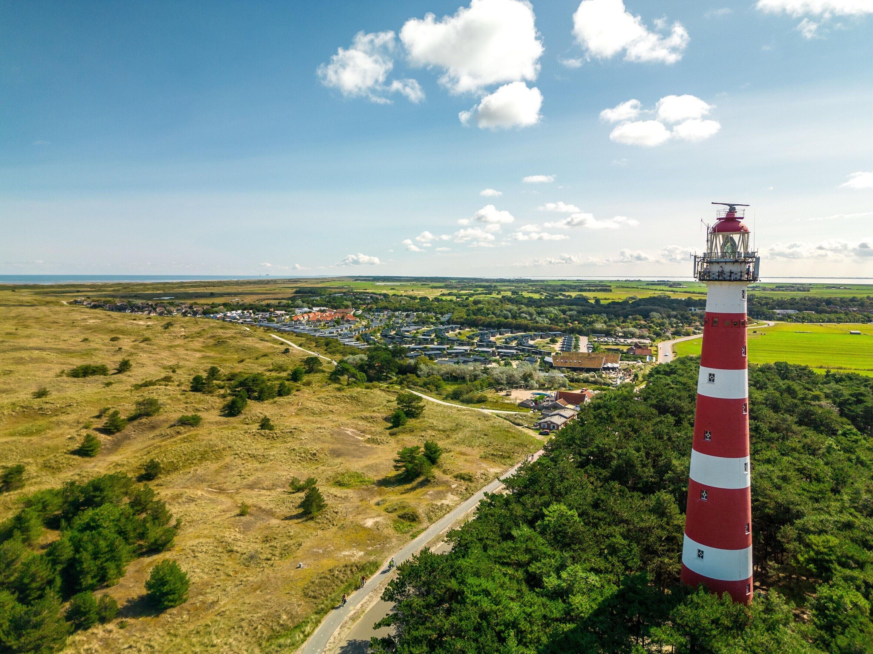 Ein Leuchtturm mit einem rot-weiß gestreiften Turm, umgeben von viel Grün und einer kleinen Stadt im Hintergrund.