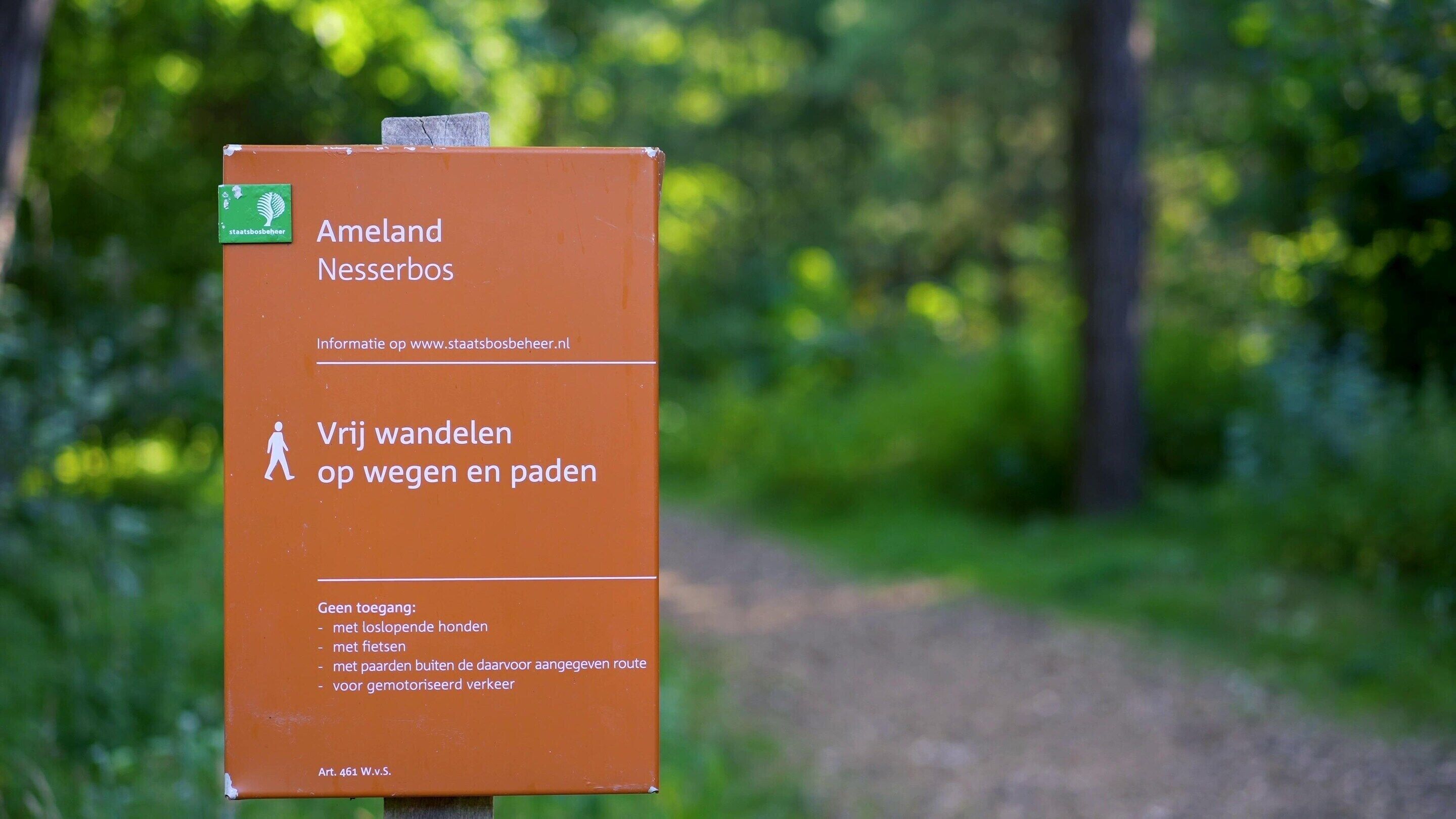A sign with the text 'Ameland Nesserbos' and 'Vrij wandelen op weg en pad' indicating a walking path.