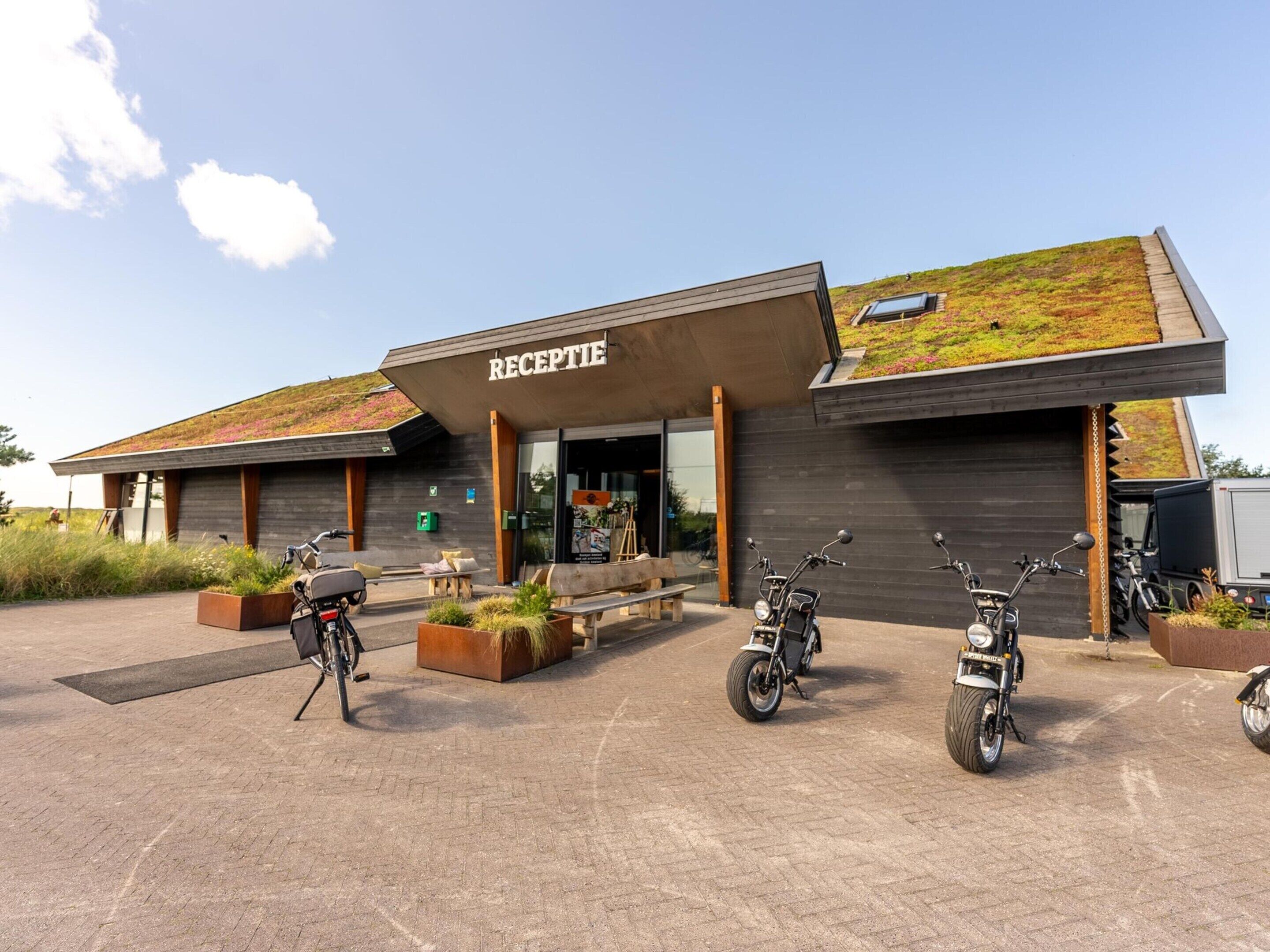 En modern byggnad med en reception, ett grönt tak och flera parkerade motorcyklar.