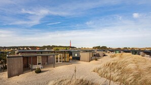 Un complexe hôtelier moderne situé en bord de mer, doté de plusieurs chalets, d’un espace de détente en plein air et d’un phare en arrière-plan.