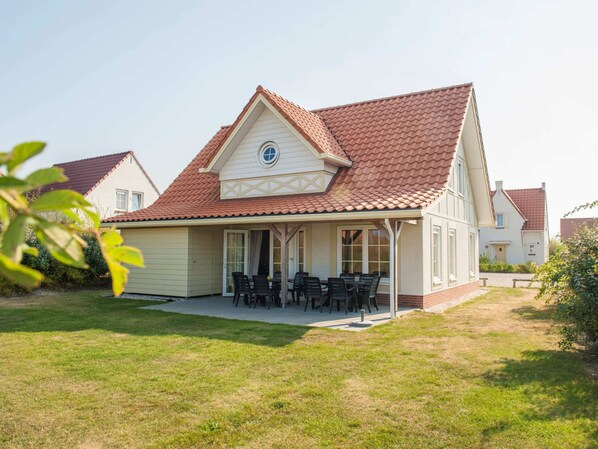 A two-story house with a red-tiled roof, a covered patio with outdoor furniture, and a well-maintained lawn. - Detached Villa With Four Bathrooms Near the Sea (Cadzand-Bad)