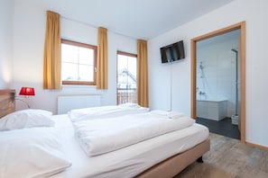 A bedroom with two beds, a TV, a red lamp, and a bathroom visible through a door. - Apartment in Obertraun Near Dachstein Ski Area (Obertraun)