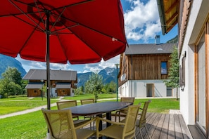 A wooden building with a balcony, a red umbrella, and a table with chairs. - Apartment in Obertraun Near Dachstein Ski Area (Obertraun)