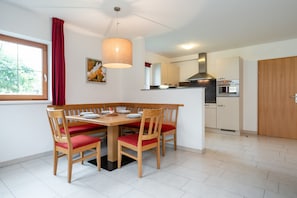 A dining area with a wooden table and chairs, a hanging light fixture, and a view of the kitchen in the background. - Apartment in Obertraun Near Dachstein Ski Area (Obertraun)