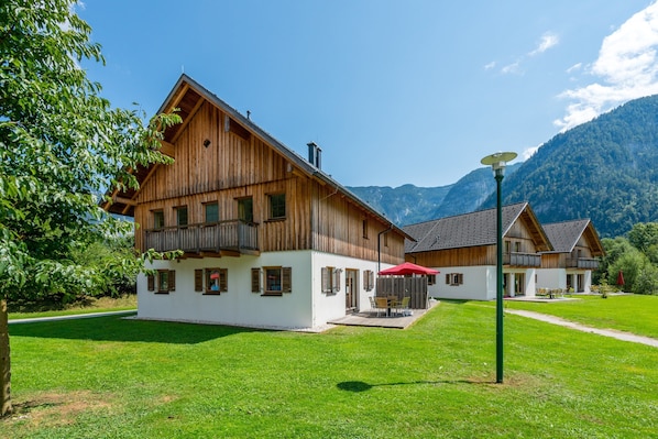 A wooden chalet with a balcony, a patio with outdoor furniture, and a mountain backdrop. - Apartment in Obertraun Near Dachstein Ski Area (Obertraun)