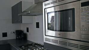 A kitchen with a stainless steel microwave, gas stove, and black coffee maker on the counter. - Holiday Home With Dishwasher, 20 km From Assen (Westerbork)