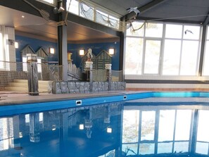 An indoor swimming pool with a clear view of the pool's edge, a stone wall, and a window with a view of trees. - Modern Chalet With Dishwasher in Noordwijk Near the Sea (Noordwijk)