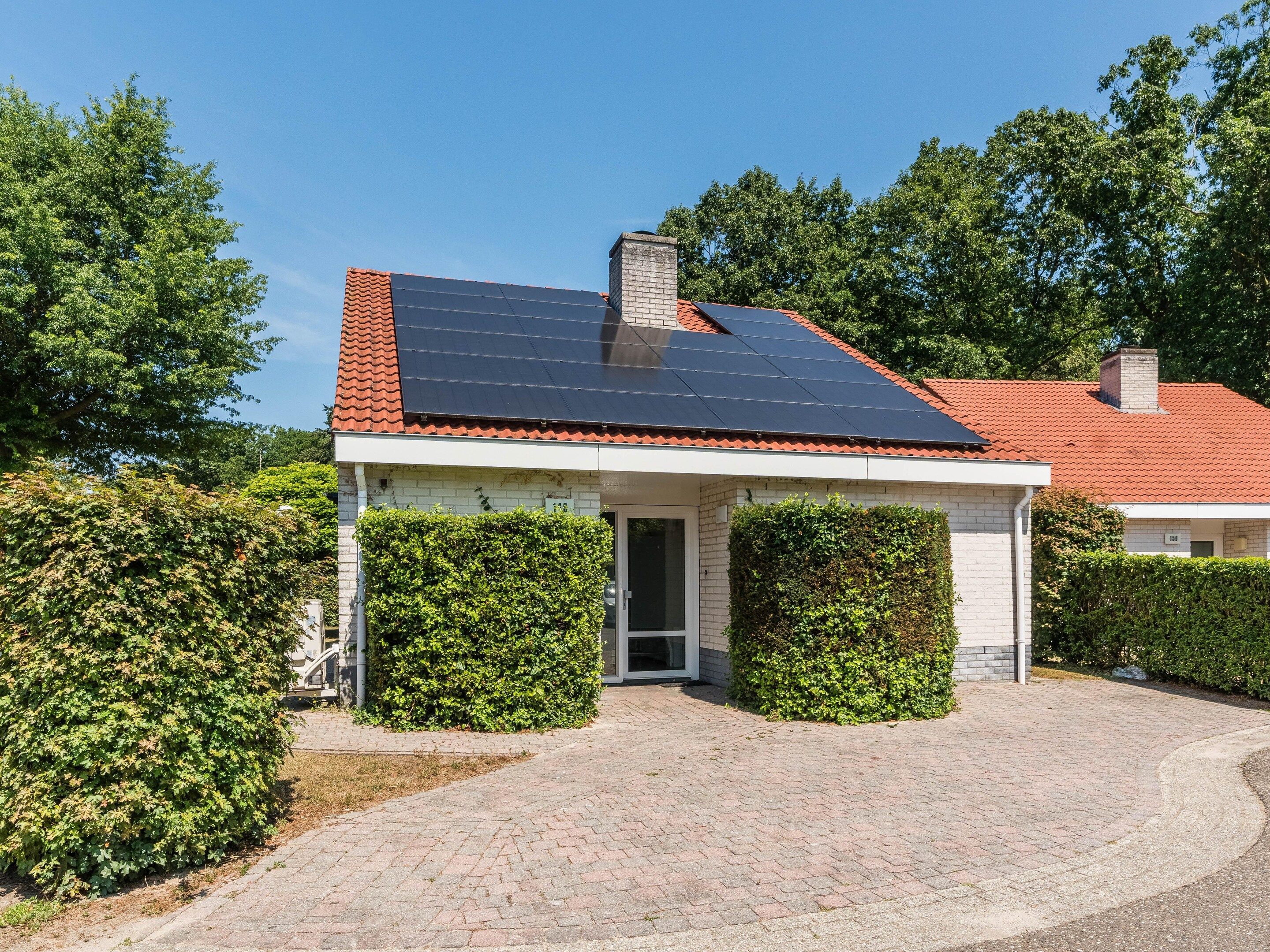 Uma casa com painel solar no telhado, chaminé de tijolos e entrada pavimentada.