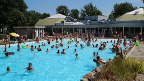 A large outdoor swimming pool surrounded by a stone wall and trees. - Modern Villa With Wellness in Limburg (Roggel)