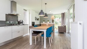 A modern kitchen with a dining area, featuring a wooden table and chairs, pendant lights, and a view of the outdoors. - Modern Villa With Wellness in Limburg (Roggel)