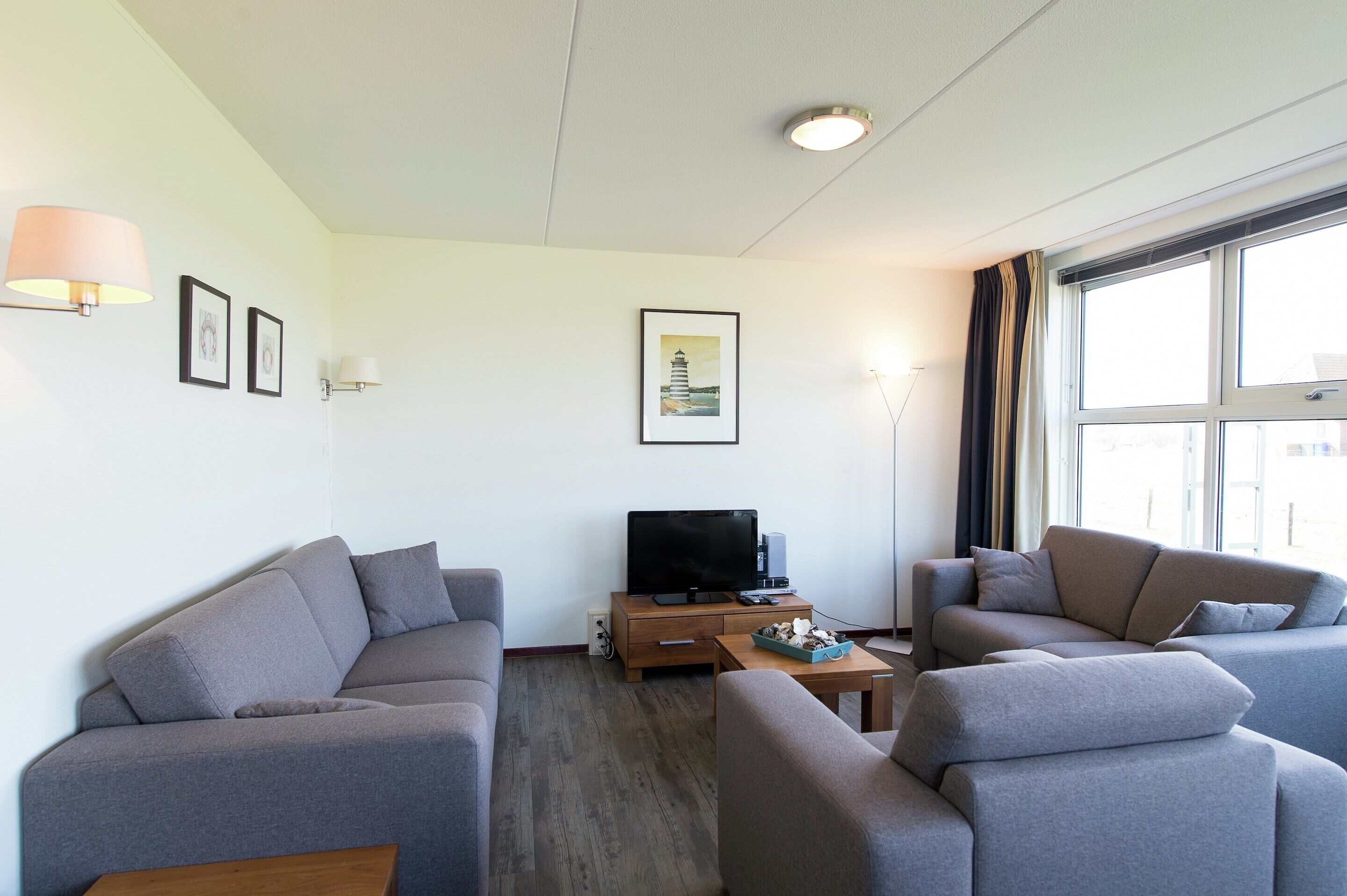 A modern living room with grey sofas, a wooden coffee table, a flat-screen TV, and a framed picture on the wall.