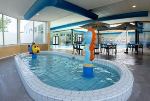 Une piscine décorée avec des motifs d’hippocampes, un espace dédié au bronzage avec des parasols, et une vue sur l’extérieur.