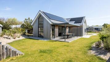 A modern house with a sloped roof, a patio with outdoor furniture, and a well-maintained lawn.
