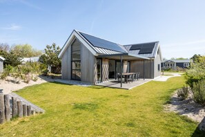 Ein modernes Haus mit Satteldach, einer Terrasse mit Gartenmöbeln und einem gepflegten Rasen.