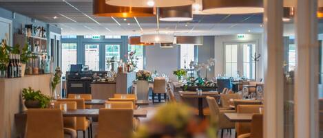 A modern restaurant with a bar area, multiple dining tables, and chairs.
