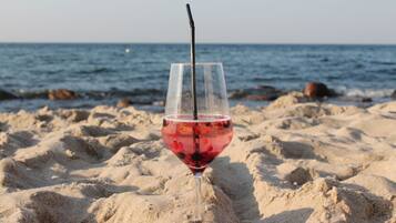 Ein Glas rotes Getränk mit einem Strohhalm an einem Sandstrand, im Hintergrund der Ozean.