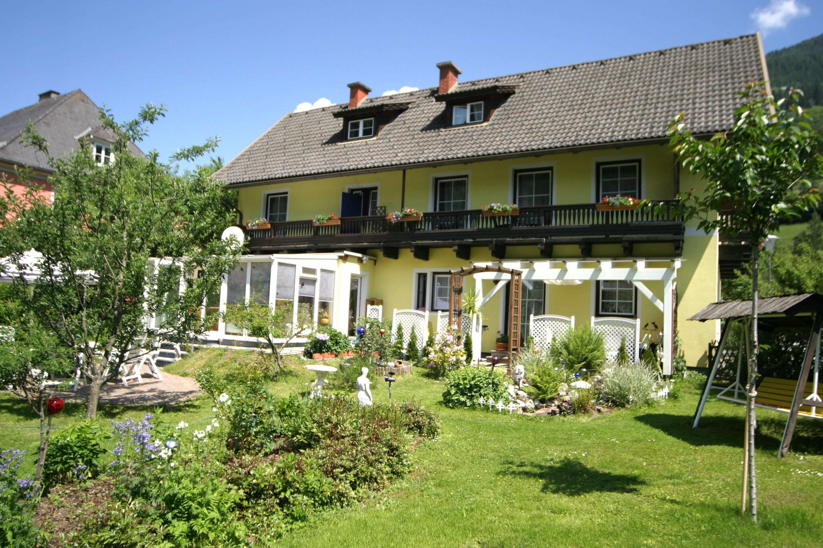 Et toetagers hus med balkon, have med forskellige planter og et hvidt hegn.