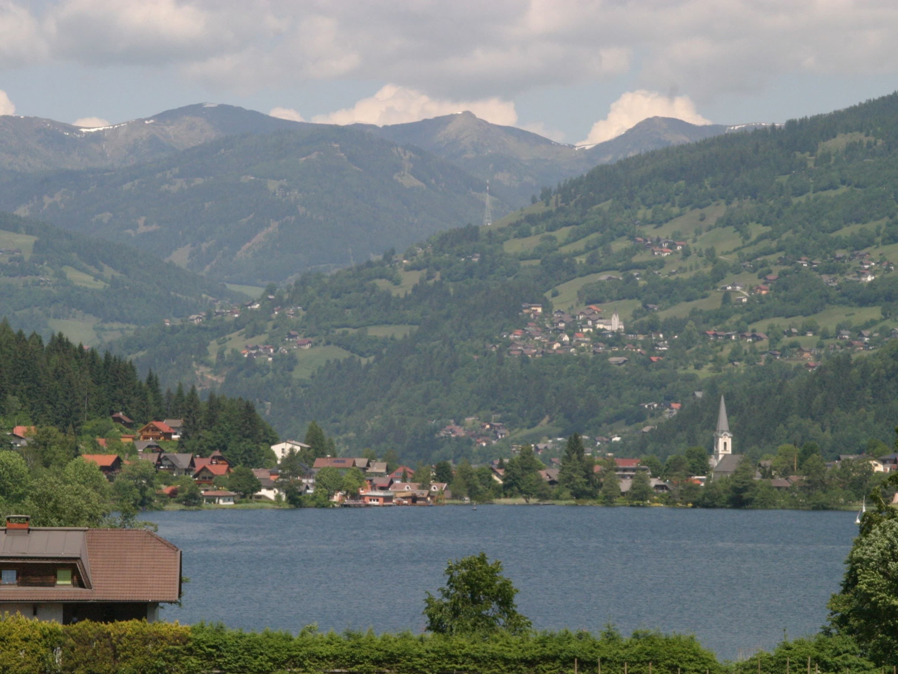 Uma vila à beira de um lago, com casas e uma igreja, rodeada por montanhas.