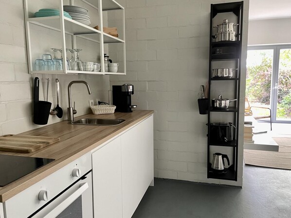 A modern kitchen with white cabinetry, a wooden countertop, a built-in sink, and a black shelving unit with kitchenware. - Idyllische Wohnung in der Nahe des Saaler Boddens (Saal)