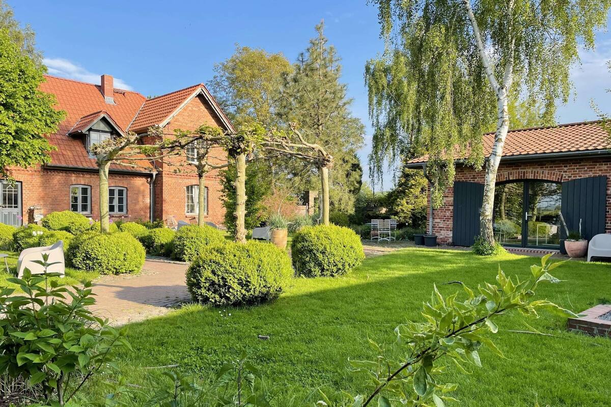 A brick house with a red-tiled roof, surrounded by well-maintained hedges and a grassy lawn.