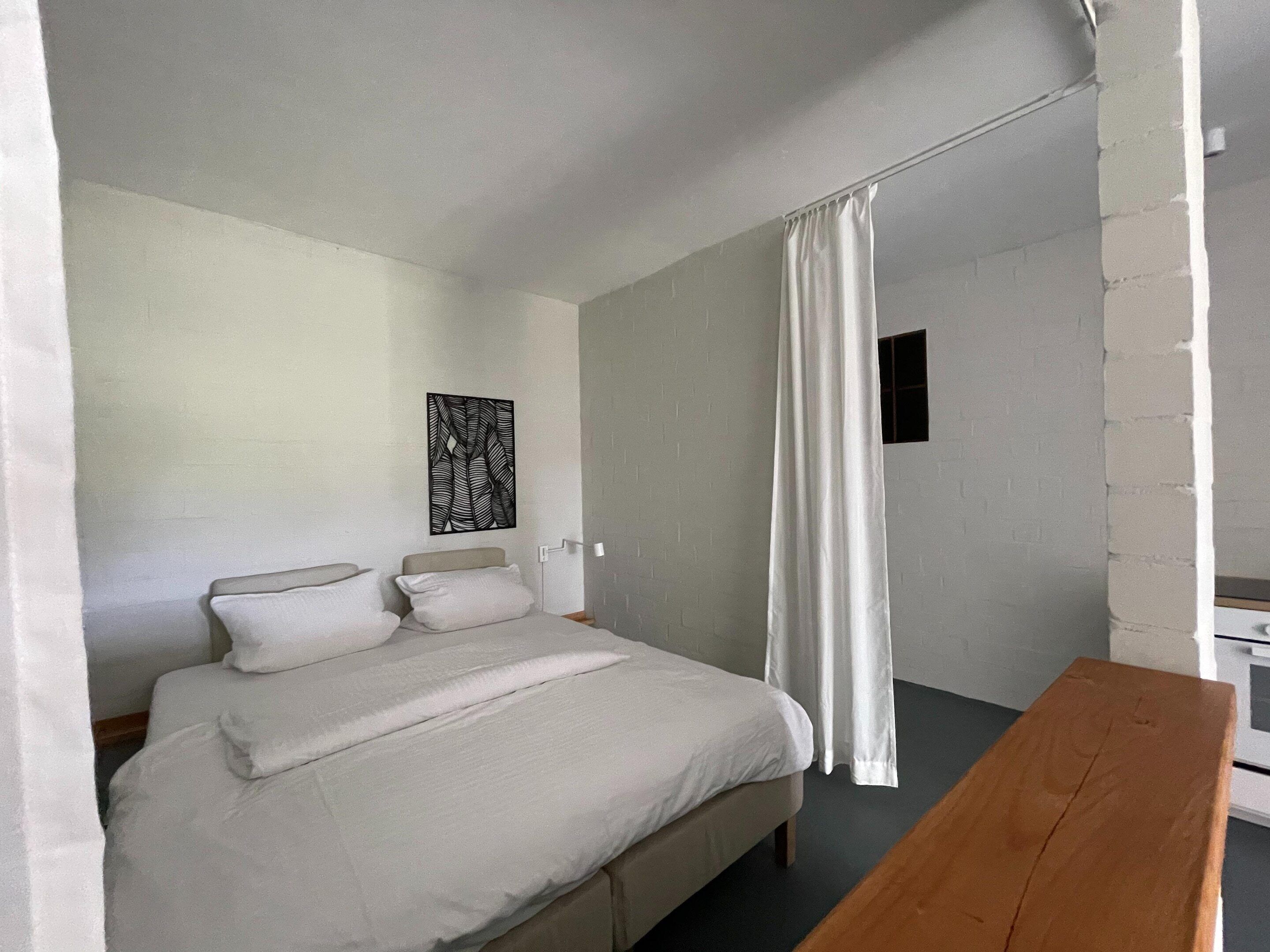 A bedroom with a bed, a bedside table, a wall-mounted artwork, and a window with curtains.