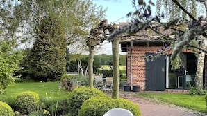 A garden with a paved path, a white plastic chair, and a brick building with a dark door. - Idyllische Wohnung in der Nahe des Saaler Boddens (Saal)