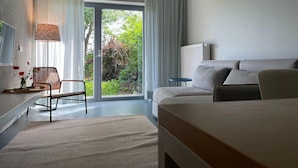 A modern hotel room with a large sliding glass door to a garden, a sofa, a chair, a small table, and a lamp. - Idyllische Wohnung in der Nahe des Saaler Boddens (Saal)