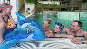 Una piscina interior con un flotador con forma de delfín, suelo de baldosas y un indicador de profundidad visible.