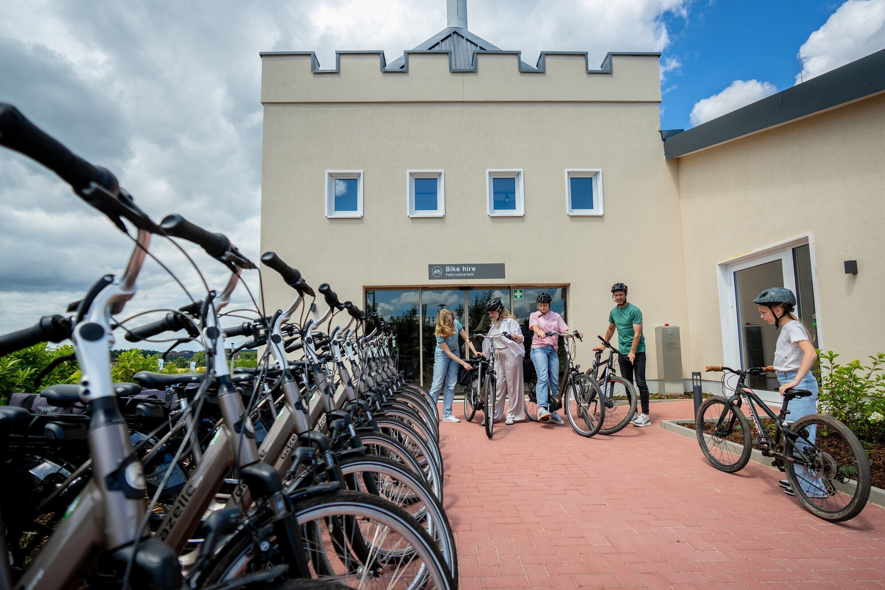 Una stazione di noleggio biciclette con una fila di biciclette e un edificio con un cartello che riporta la scritta 'Bike hire'.