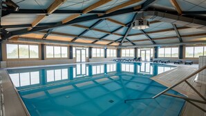 En indendørs swimmingpool med klart blåt vand, træbjælker og store vinduer.
