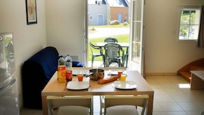 A dining area with a table set for two, a sofa, and a view of the outside. - Brittany Retreat w/ Pool (Le Tronchet)