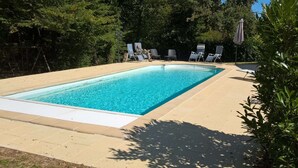 Ein rechteckiger Pool mit Fliesen umgeben, umgeben von Bäumen und beschattet durch einen großen Sonnenschirm.