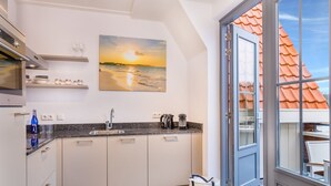 Een moderne keuken met witte kasten, een granieten aanrechtblad en een groot raam met uitzicht op een gebouw met rode dakpannen.
