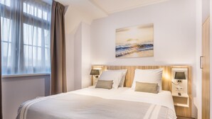 Een moderne hotelkamer met een groot bed, twee nachtkastjes met lampen, een schilderij aan de muur en een raam met gordijnen.