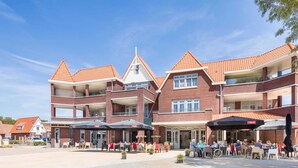 Een meerlaags gebouw met een rode pannendak, een terras en een overdekte patio.