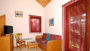 A living room with a sofa, a television on a wooden cabinet, a chair, a small table, and two windows with curtains. - Spacious Alpine Chalet (Le Dévoluy)