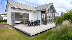 Una casa moderna con un gran ventanal que da a un patio con mesa y sillas.