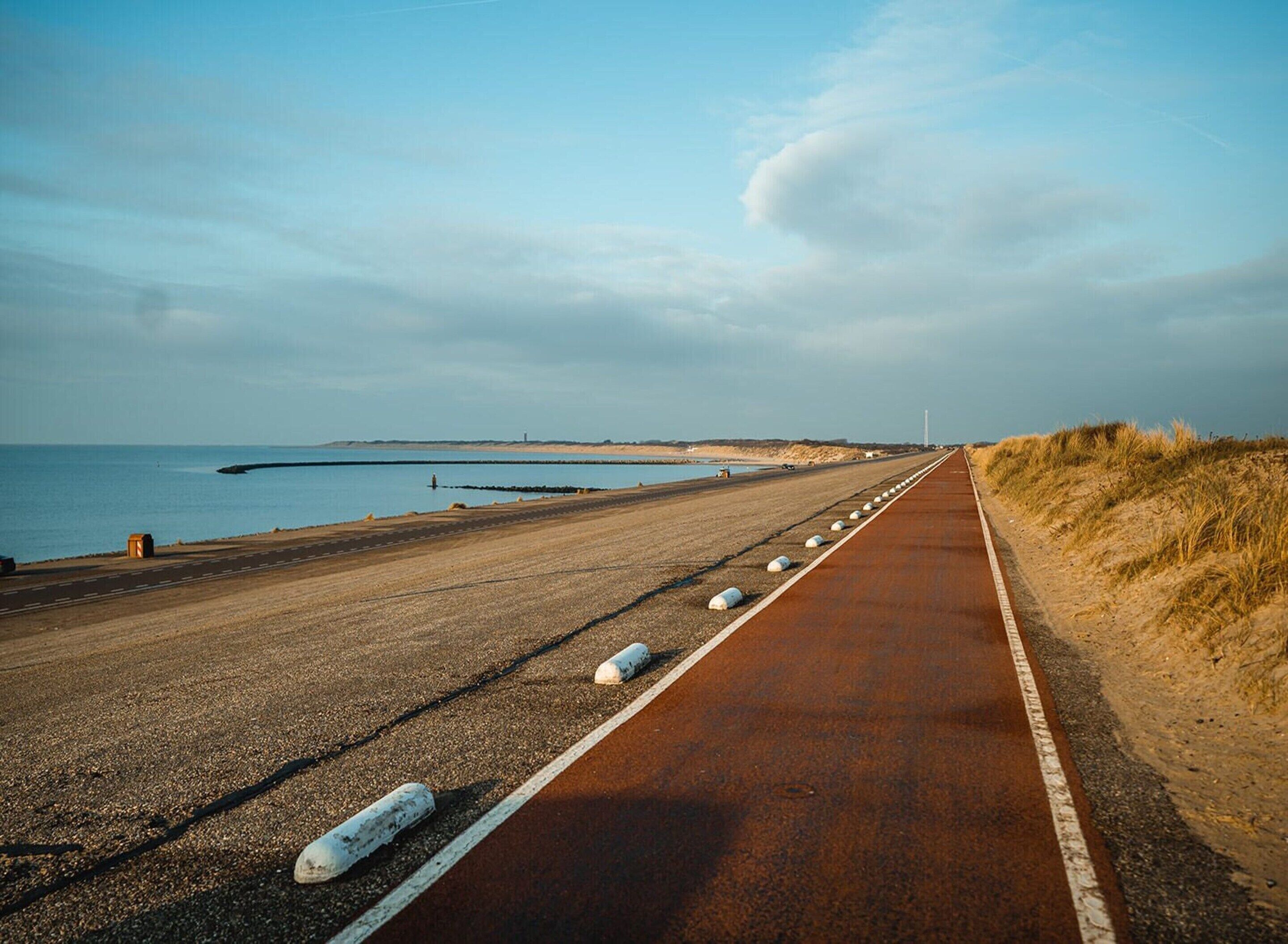 A coastal road with a sandy shoulder and a paved path.