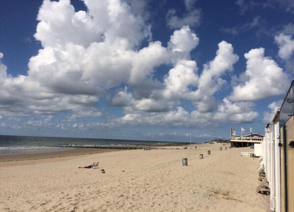A beach with a pier extending into the sea, a sandy shore, and a building with flags. - Zoutelande Studio + Parking Spot (Zoutelande)