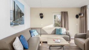 Egy modern nappali, melyben bézs színű kanapé, egy dohányasztal és egy móló képét ábrázoló festmény található.