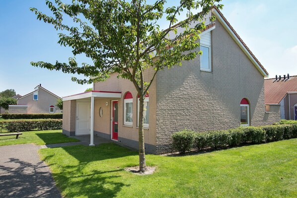 A two-story building with a stone facade, a red door, and a small tree in the front yard. - Spacious Holiday Home in Renesse near North Sea (Noordwelle)