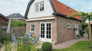 A two-story house with a red-tiled roof, white siding, and a brick exterior. There is a patio with outdoor furniture and a small garden area. - Comfortable Flat in Bergen (Bergen)