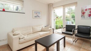A living room with a beige sofa, a dark coffee table, and two black chairs. There is a large window with a view of greenery outside. - Comfortable Flat in Bergen (Bergen)